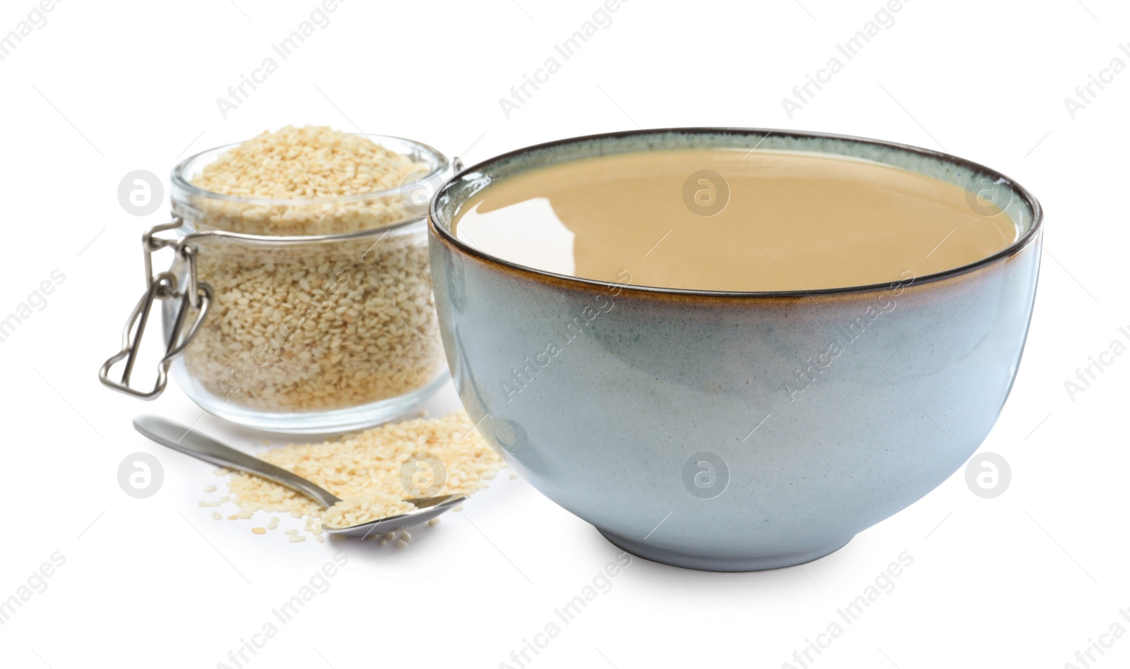 Photo of Bowl of tasty sesame paste, jar, spoon and seeds on white background