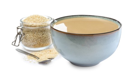 Bowl of tasty sesame paste, jar, spoon and seeds on white background