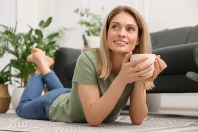 Woman holding cup of drink on floor in room with beautiful houseplants