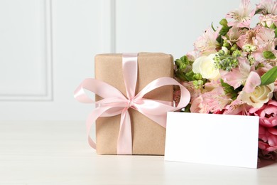 Photo of Happy Mother's Day. Gift box, blank card and bouquet of beautiful flowers on white table. Space for text