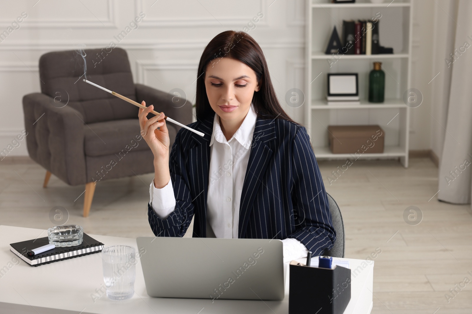 Photo of Woman using long cigarette holder for smoking at workplace in office