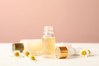 Photo of Cosmetic products and chamomiles on white table against pink background