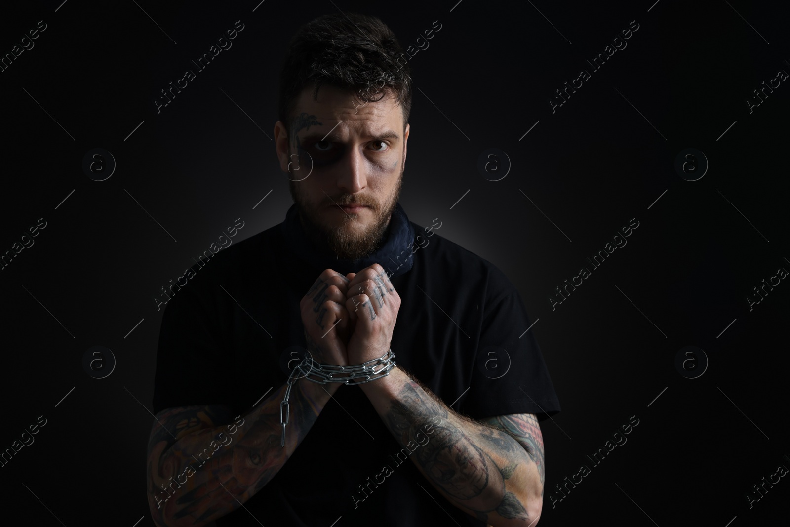 Photo of Man with bruise chained on dark background. Hostage