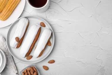 Photo of Delicious eclairs covered with glaze, coffee and almonds on white textured table, flat lay. Space for text