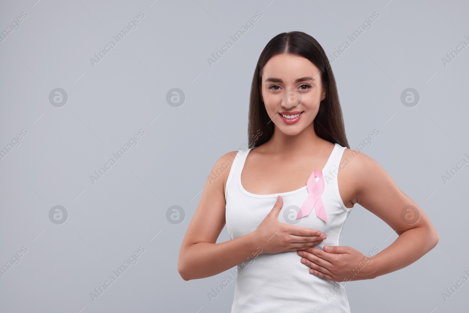 Photo of Beautiful woman with pink ribbon on light grey background, space for text. Breast cancer awareness