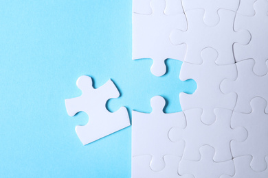 Blank white puzzle with separated piece on light blue background, flat lay