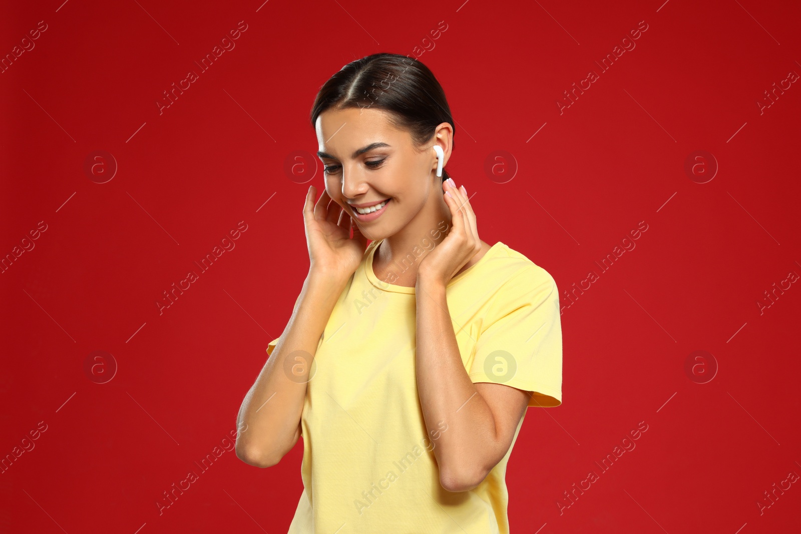 Photo of Happy young woman listening to music through wireless earphones on red background