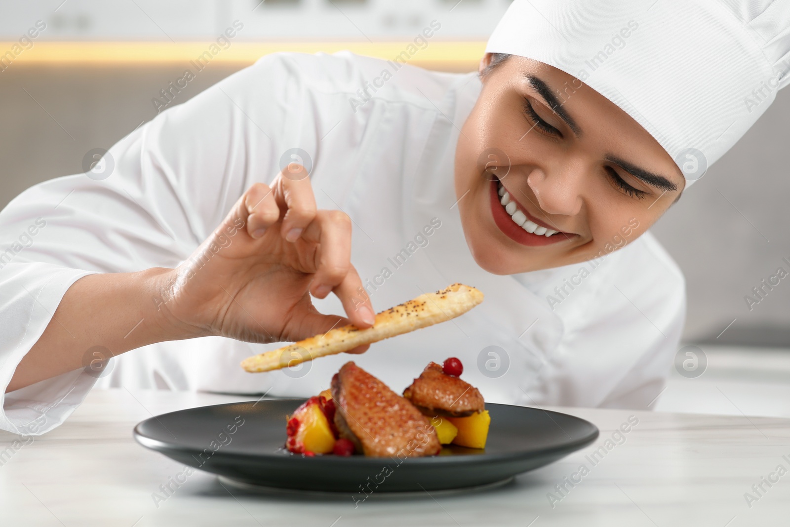 Photo of Professional chef decorating delicious dish with crispy bread at marble table