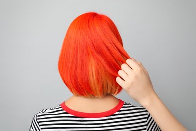 Professional stylist and young woman with bright dyed hair on grey background, back view