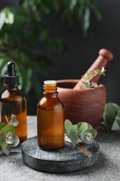 Photo of Bottles of eucalyptus essential oil, leaves and mortar on light grey table