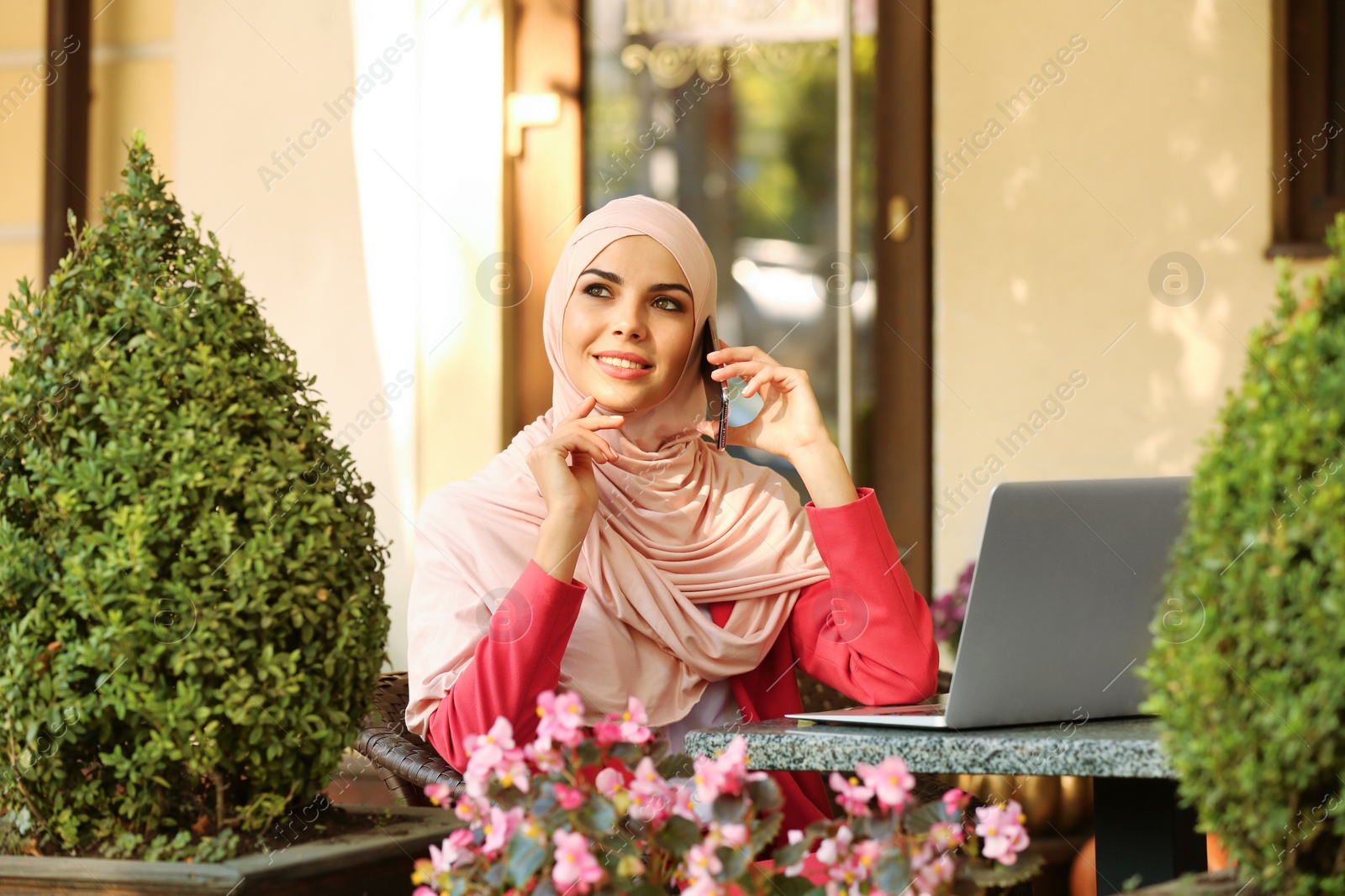 Photo of Muslim woman talking on phone in outdoor cafe