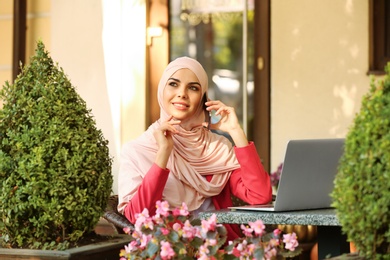 Photo of Muslim woman talking on phone in outdoor cafe