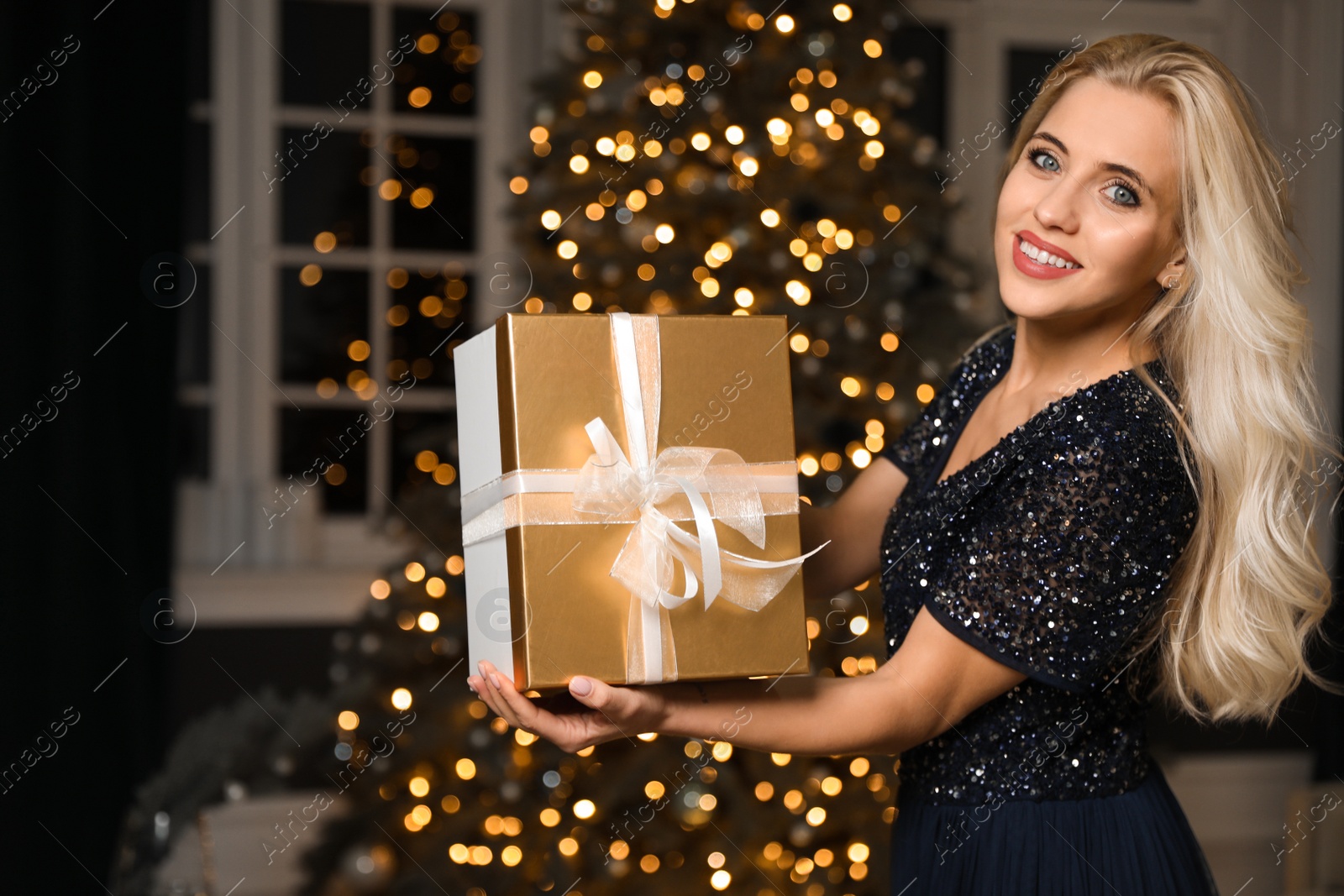 Photo of Beautiful woman with gift box in decorated room. Christmas celebration