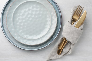 Stylish setting with cutlery, napkin and plates on white table, top view