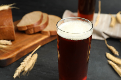Photo of Glass of delicious kvass, bread and spikes on black table