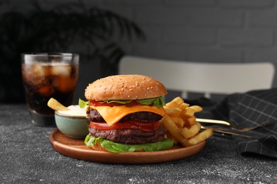 Photo of Tasty cheeseburger with patties, sauce and French fries on grey textured table