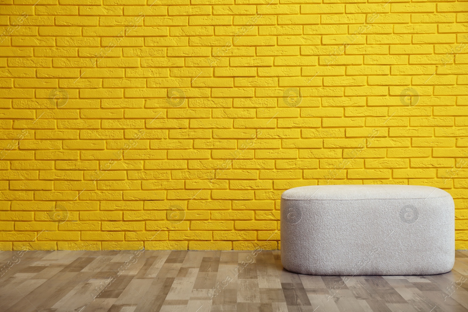 Photo of Stylish comfortable pouf near yellow brick wall, space for text. Interior design