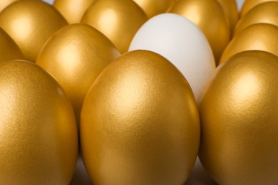 Photo of Ordinary chicken egg among golden ones as background, closeup