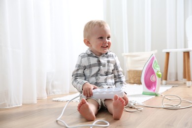 Photo of Little child playing with power strip on floor at home. Dangerous situation