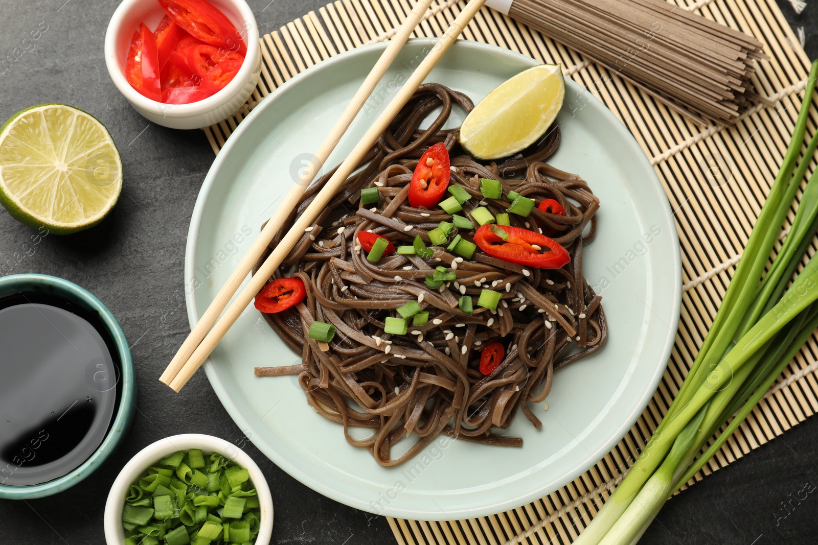 Photo of Tasty buckwheat noodles (soba) with ingredients and chopsticks on grey table, flat lay