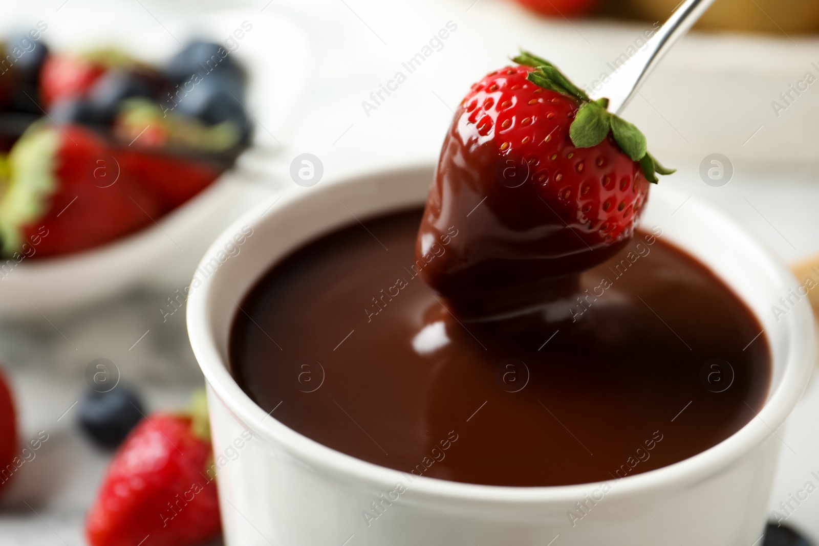 Photo of Dipping strawberry into fondue pot with chocolate, closeup