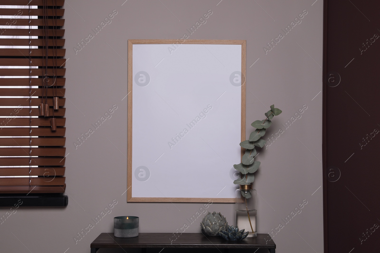Photo of Empty frame hanging on grey wall over wooden table with decor. Mockup for design