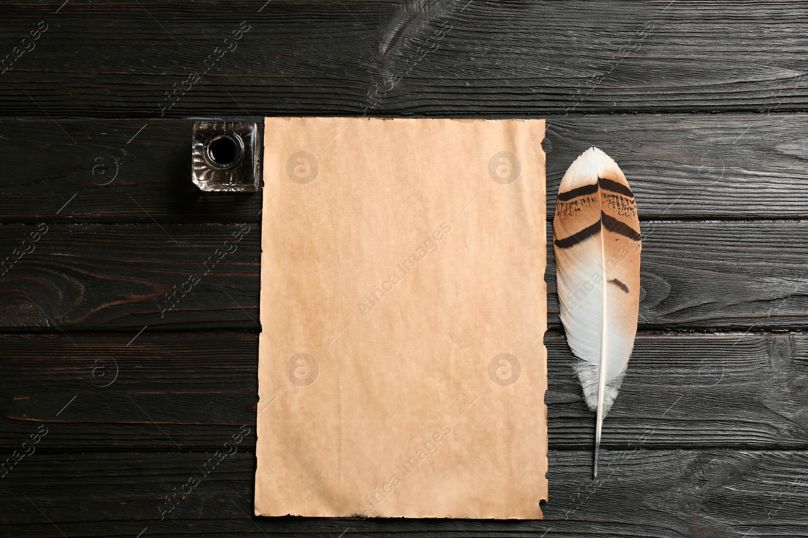 Photo of Feather pen, inkwell and blank parchment on wooden table, top view. Space for text