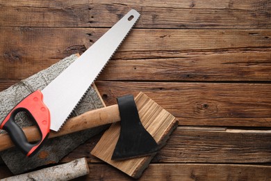 Saw with colorful handle, axe and logs on wooden background, flat lay. Space for text