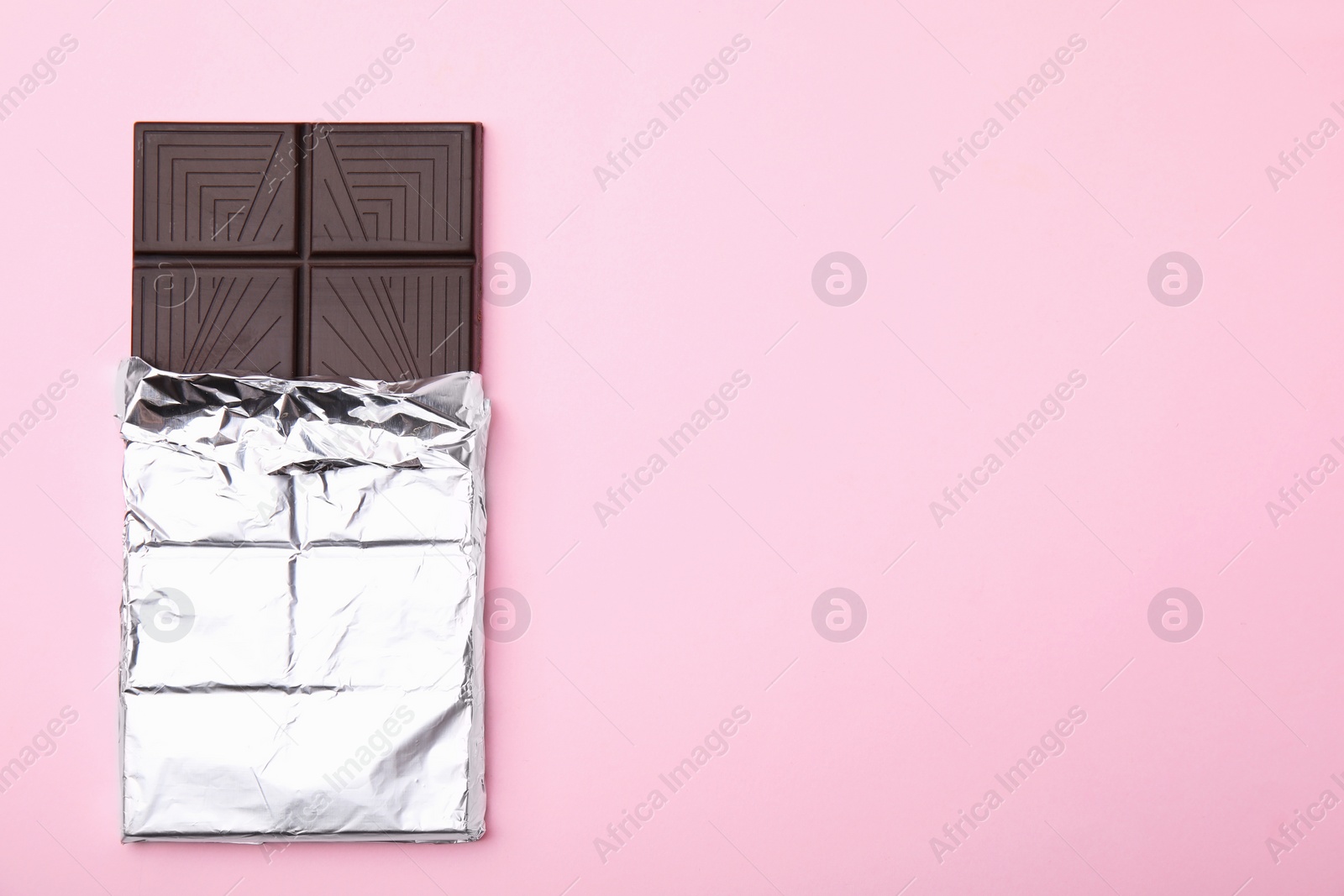 Photo of Tasty chocolate bar on pink background, top view. Space for text