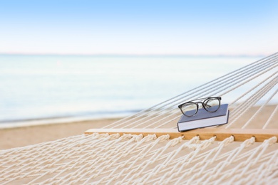 Photo of Comfortable hammock with book and glasses at seaside