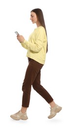 Photo of Young woman in casual outfit using smartphone while walking on white background