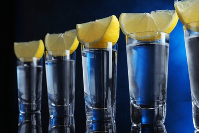 Shot glasses of vodka with lemon slices on dark blue background