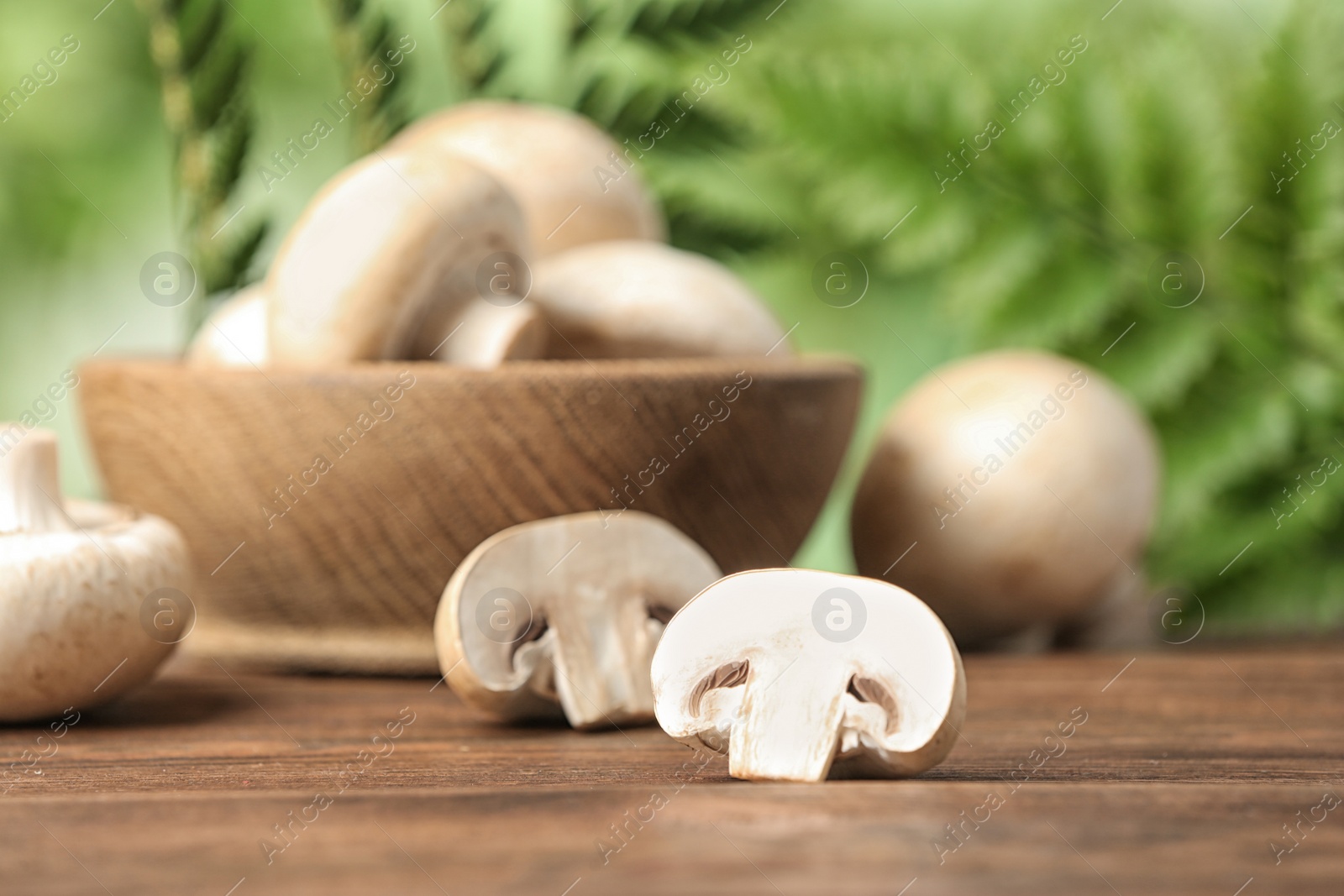 Photo of Fresh champignon mushrooms on wooden table against blurred background