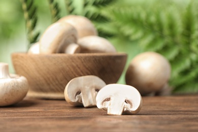 Photo of Fresh champignon mushrooms on wooden table against blurred background