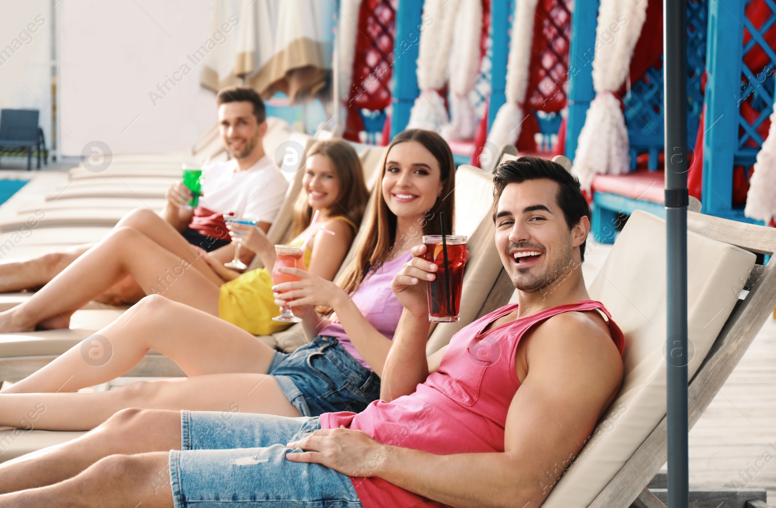 Photo of Happy young friends with fresh summer cocktails relaxing on sunbeds