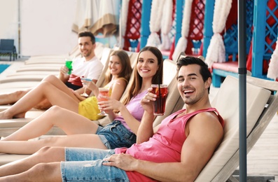 Photo of Happy young friends with fresh summer cocktails relaxing on sunbeds