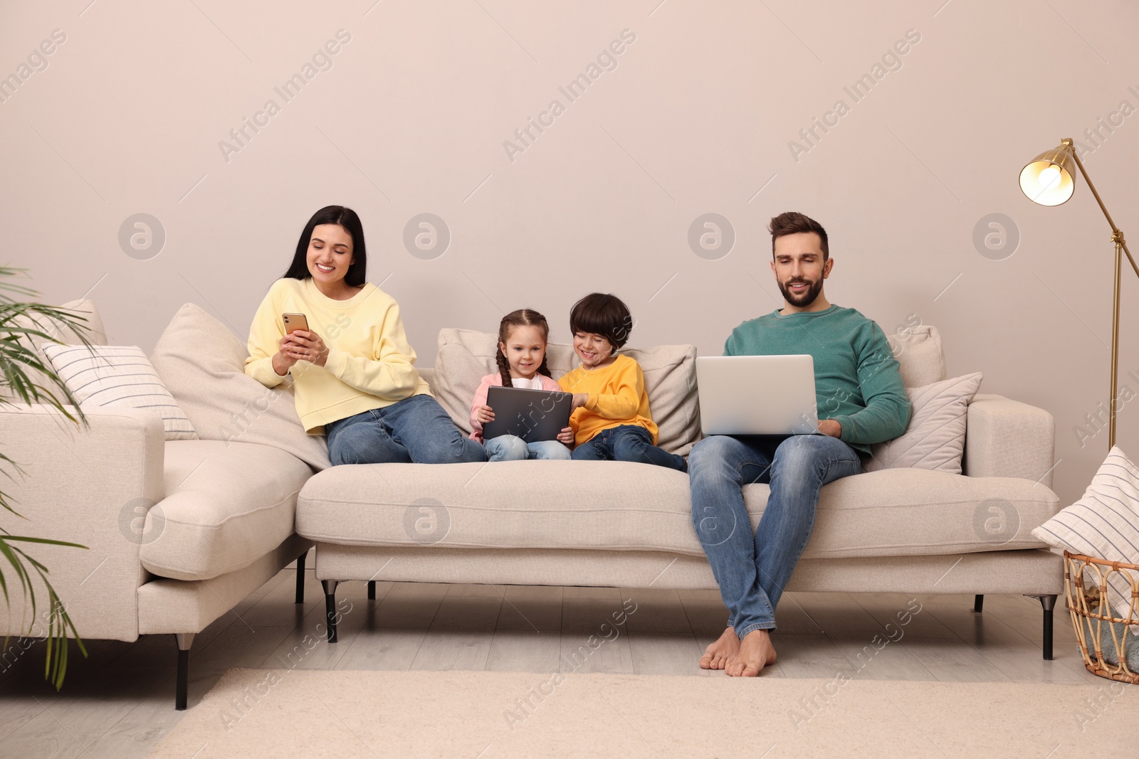 Photo of Happy family with gadgets on sofa in living room