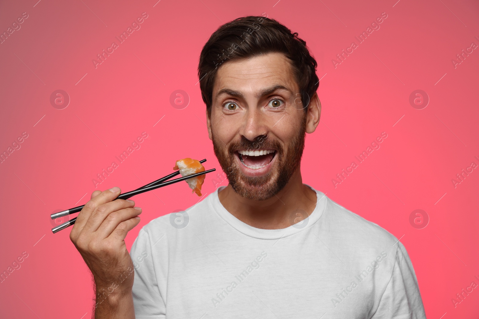 Photo of Emotional man holding tasty sushi with chopsticks on pink background