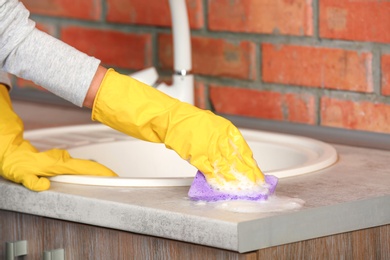 Photo of Woman cleaning counter with sponge in kitchen, closeup
