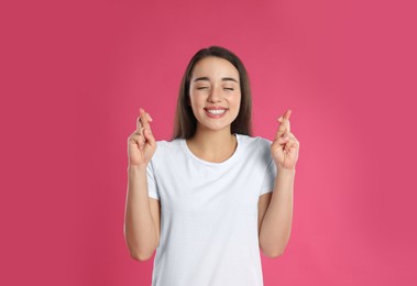 Photo of Woman with crossed fingers on pink background. Superstition concept