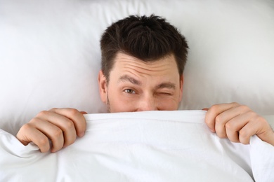 Photo of Handsome man covering his face with blanket while lying on pillow, top view. Bedtime