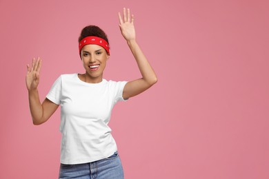 Photo of Happy young woman in stylish headband dancing on pink background. Space for text
