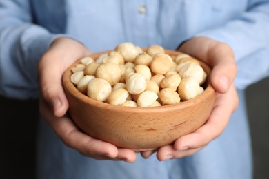 Photo of Woman holding bowl with shelled organic Macadamia nuts, closeup