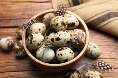Speckled quail eggs and feathers on wooden table, above view
