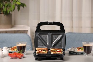 Photo of Modern grill maker with sandwiches and coffee on light grey table indoors