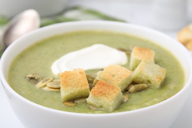 Delicious broccoli cream soup with croutons, sour cream and pumpkin seeds in bowl, closeup