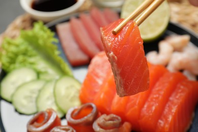 Photo of Taking tasty salmon slice with chopsticks above plate, closeup. Delicious sashimi dish