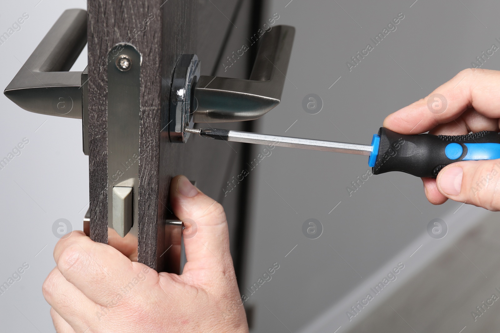 Photo of Handyman with screwdriver repairing door handle indoors, closeup