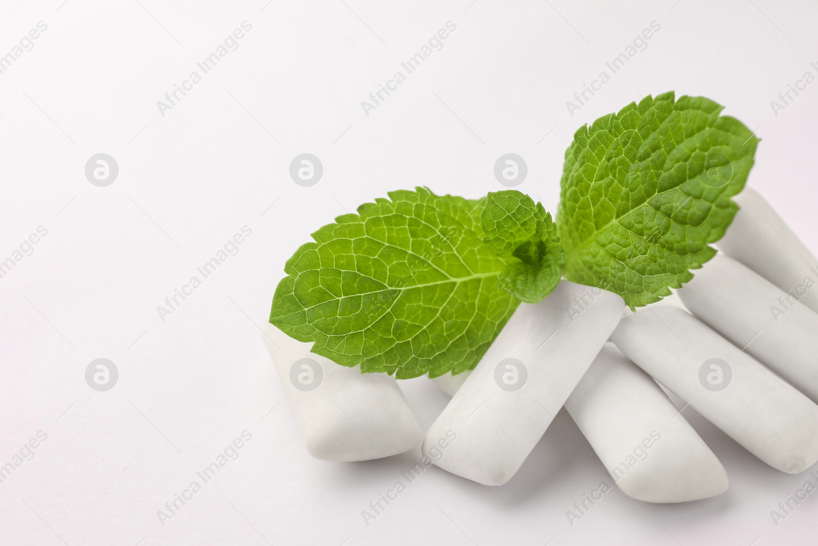 Photo of Tasty chewing gums and mint leaves on white background, closeup. Space for text