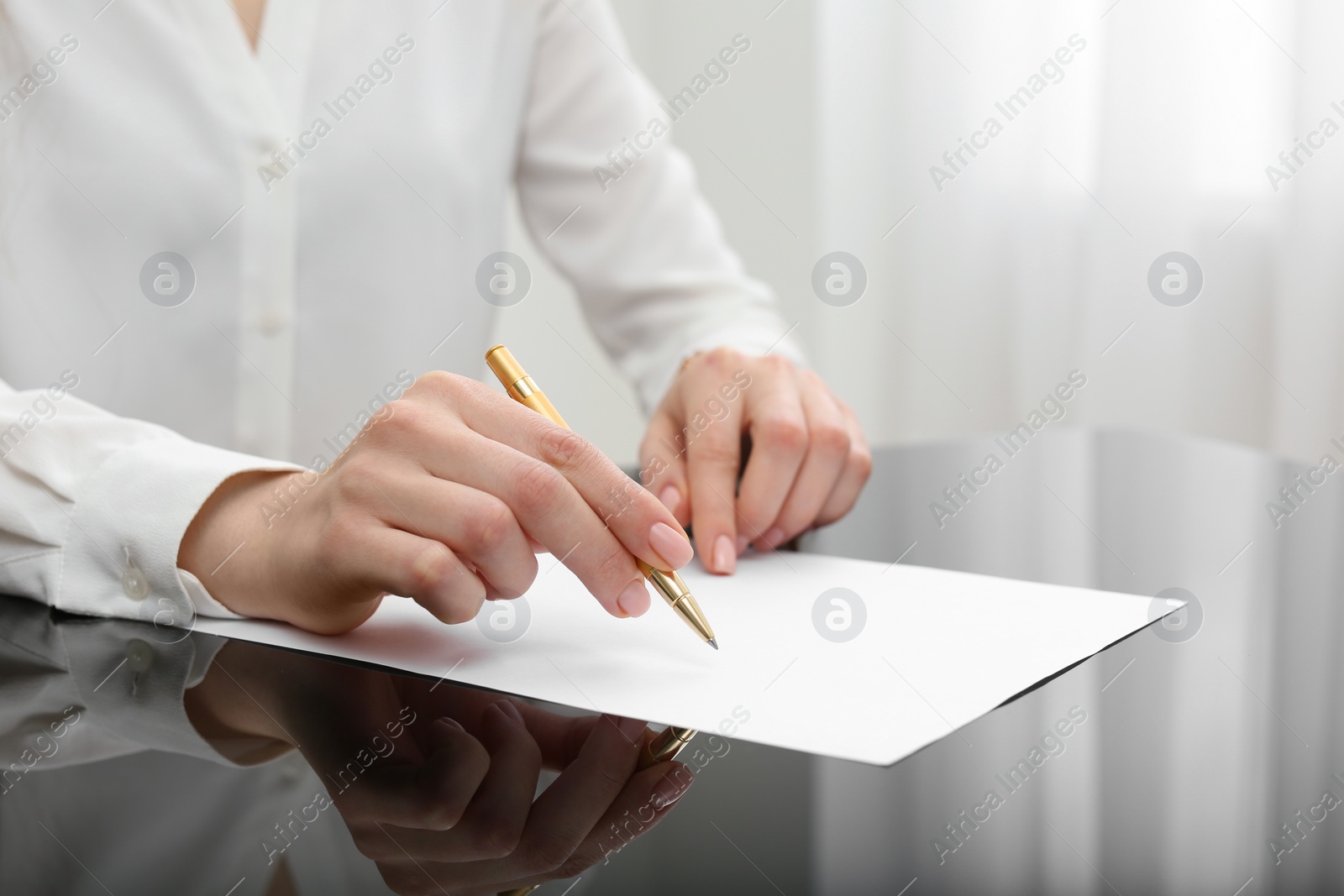 Photo of Woman writing on sheet of paper at glass table, closeup